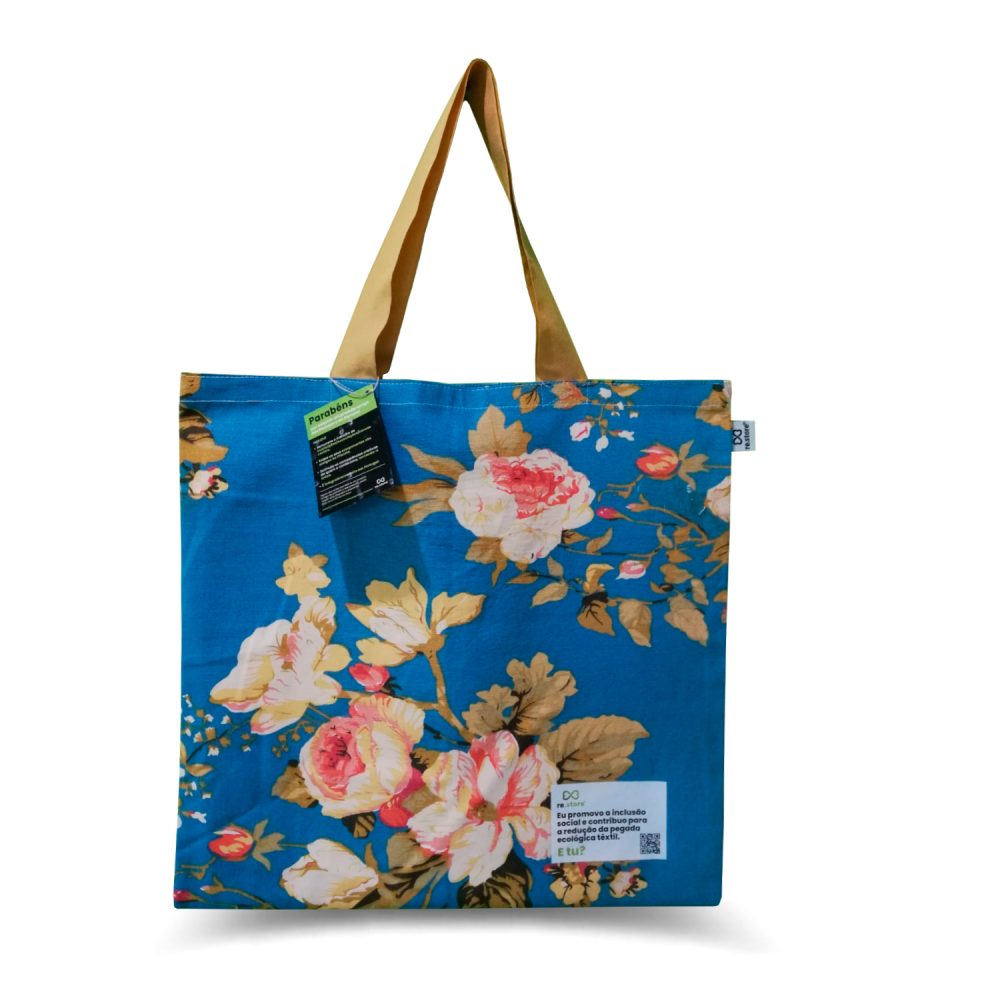 Saco de compras azul com flores em tons de amarelo e rosa. Alça dourada